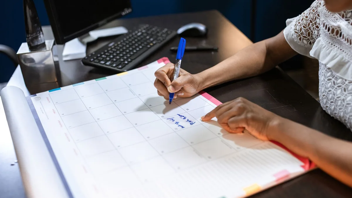Persona anotando fechas en un calendario de sobremesa sobre una mesa de trabajo